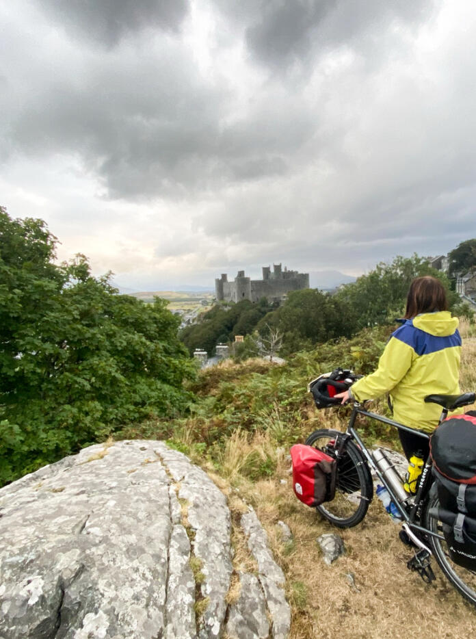 Person steht mit Fahrrad und blickt auf die Landschaft mit der Burg in der Ferne.