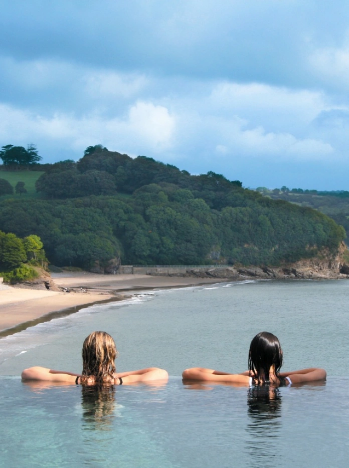 Zwei Frauen entspannen sich im Schwimmbecken des St. Brides Spa Hotel und blicken auf den Strand.