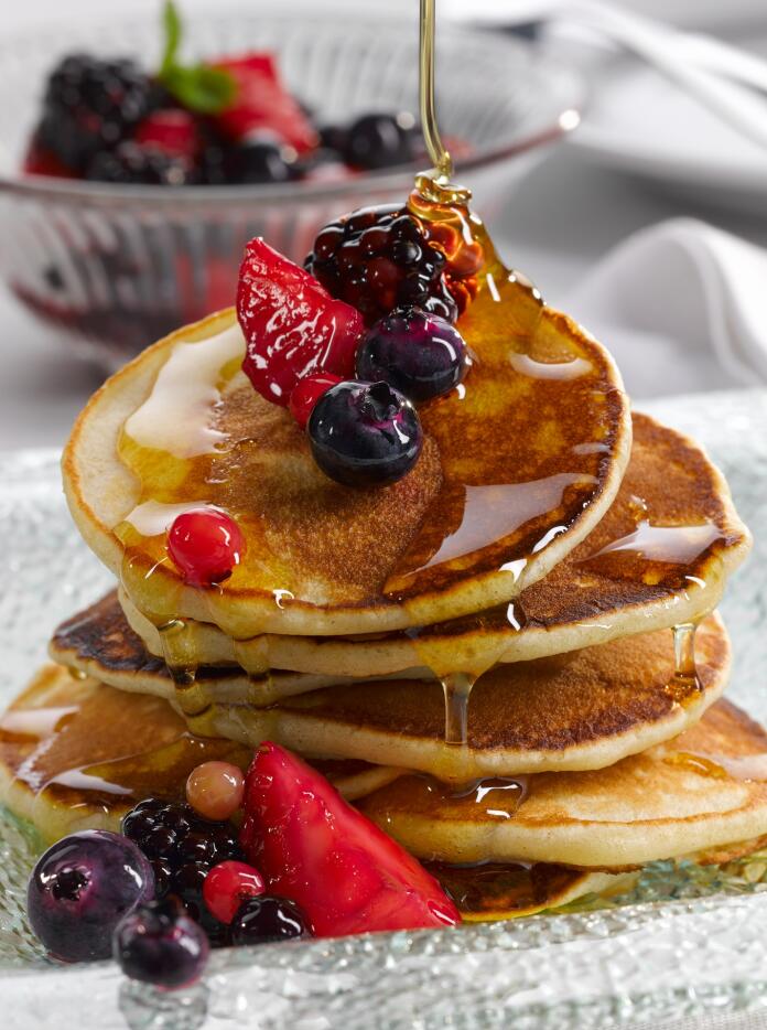 A pile of crempog (pancakes) with berries and syrup.