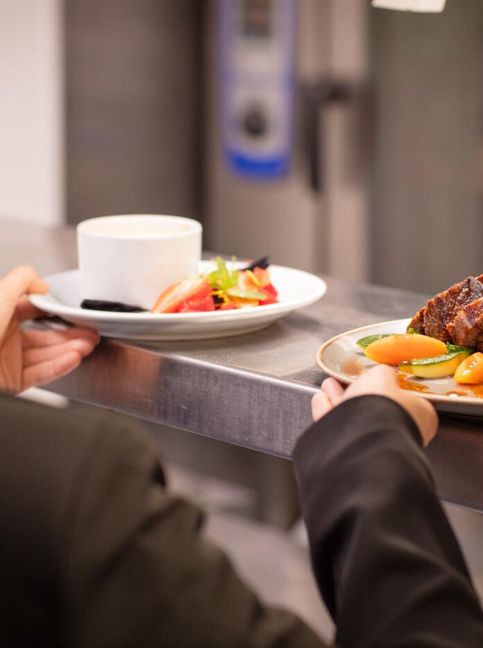 Speisen in einem Restaurant, die von einer Bedienung in der Küche entgegengenommen werden.