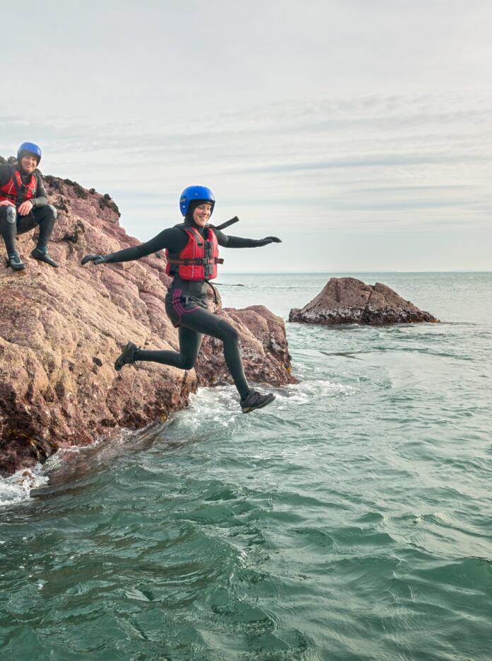 Woman jumping into the sea, coasteering in Pembrokeshire.