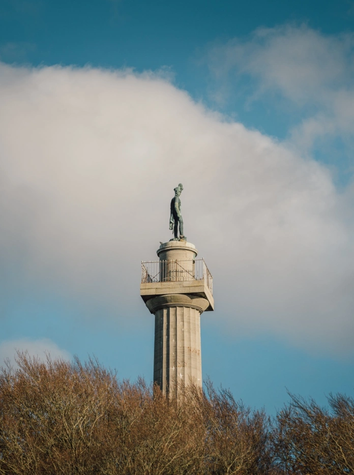 A tall pale stone column with a viewing platform and statue at the top.