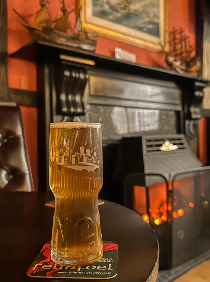 A pint of lager on a table in front of a lit stove in a pub.