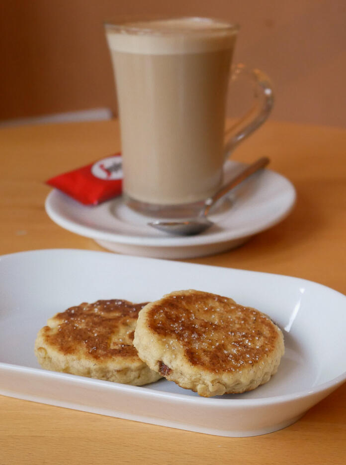 Two Welsh cakes on a white plate, next to a milky coffee.