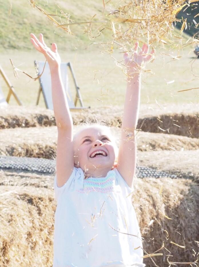 girl holding hands above her head, with bales of straw in background.