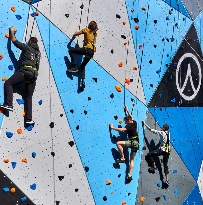 People wearing safety harnesses scaling a climbing wall in an adventure parc.