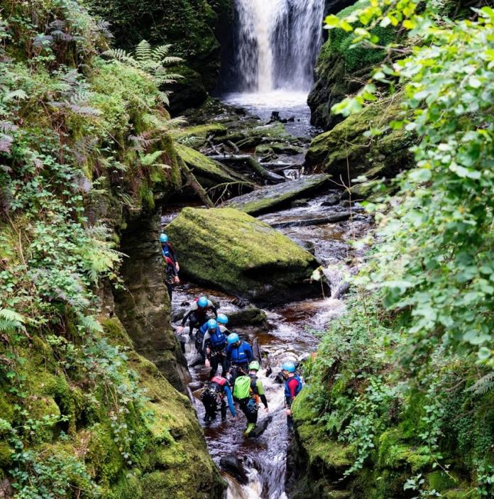 A group of people in wet gear climbing the rocks near a waterfall.