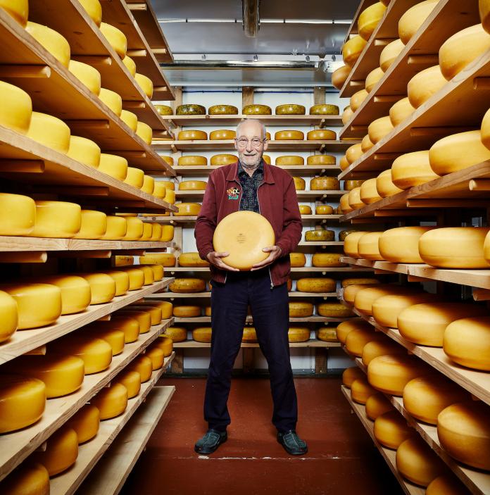 John Savage-Onstwedder of Caws Teifi cheese holding cheese stands surrounded by cheese on shelves