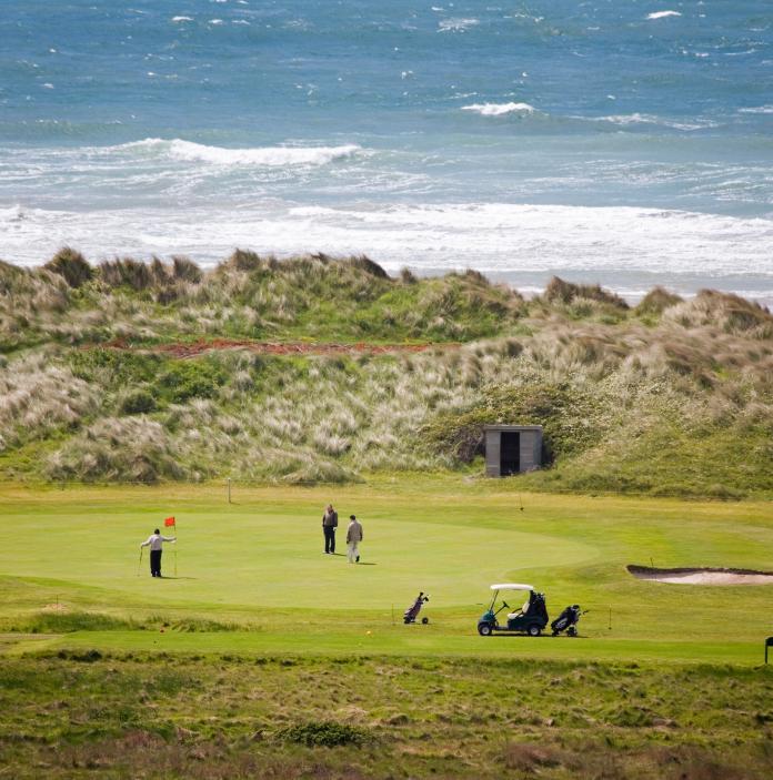 people playing golf on a green with the sea in the background