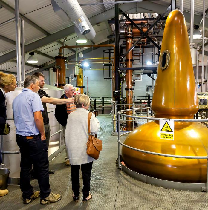 A group of visitors on a Penderyn Distillery tour with a guide looking at the yellow gold vats.