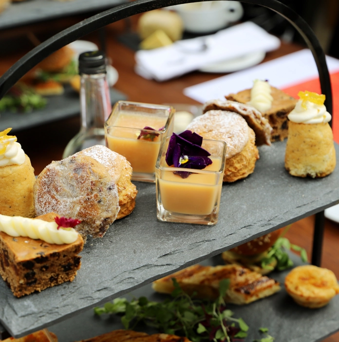 An afternoon tea of cakes and savouries on a slate tray.