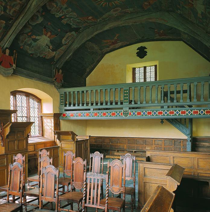 interior of chapel with decorative ceiling and balcony and wooden furniture.