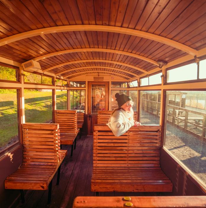 A person sat in an open wooden railway carriage.