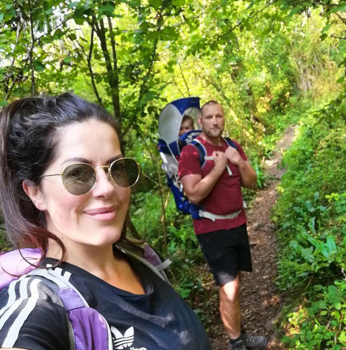 A woman, man and baby in a carrier walking along a woodland path.