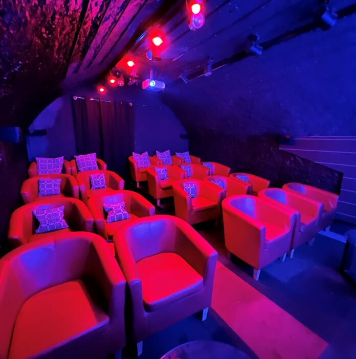 Inside a dark underground cinema with comfortable tub chairs and cushions. 