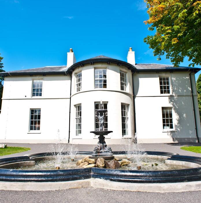 A white painted Regency house with a fountain in front.