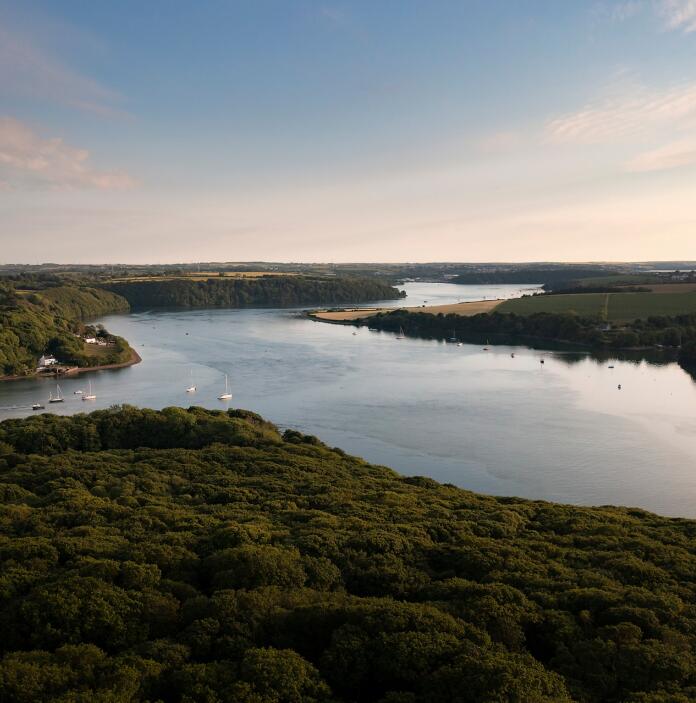 Aerial view of an estuary surrounded by green woodland.