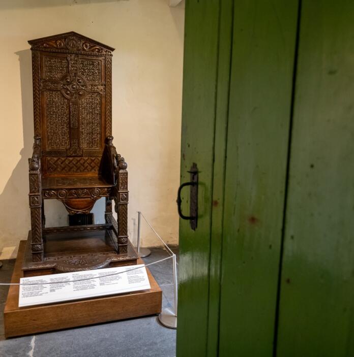 A wooden Eisteddfod chair on display behind a half-closed green wooden door. 