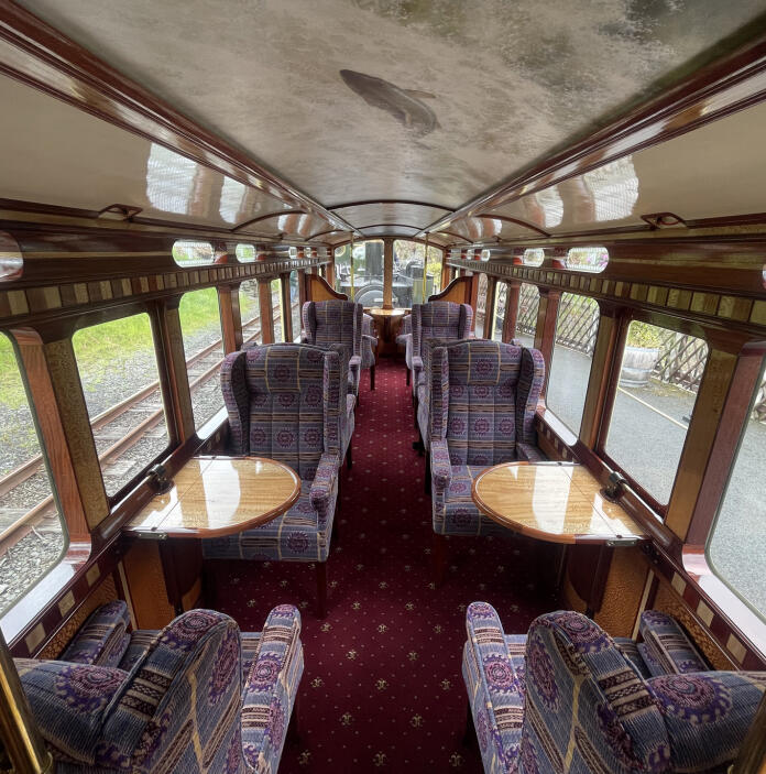 Interior of a luxury narrow gauge railway carriage with comfortable armchairs and tables.