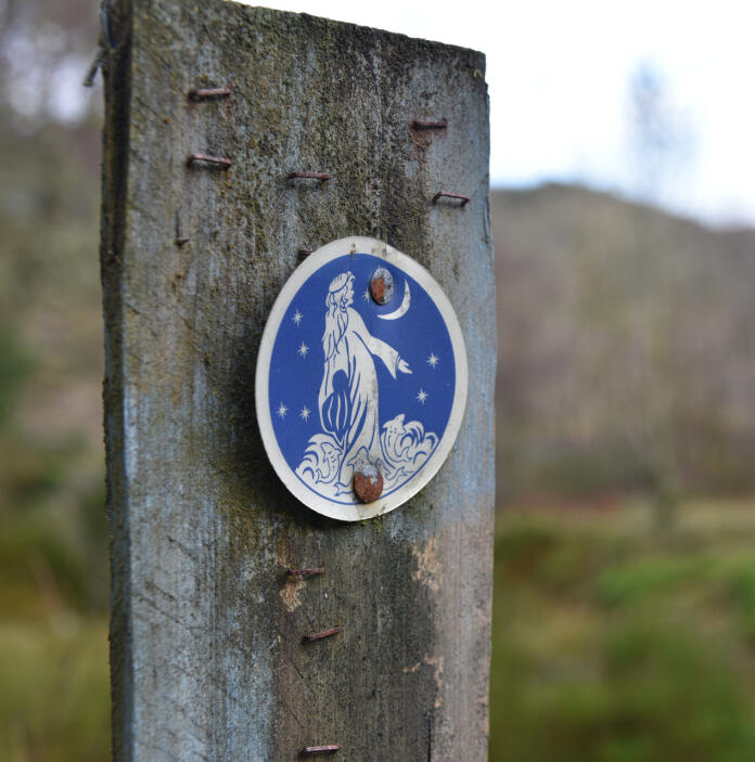 A trail waymarker showing a woman and a moon.