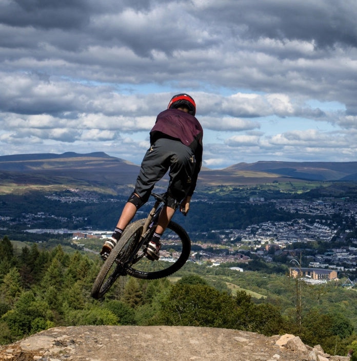 A mountain bike rider on a jump overlooking a large town.