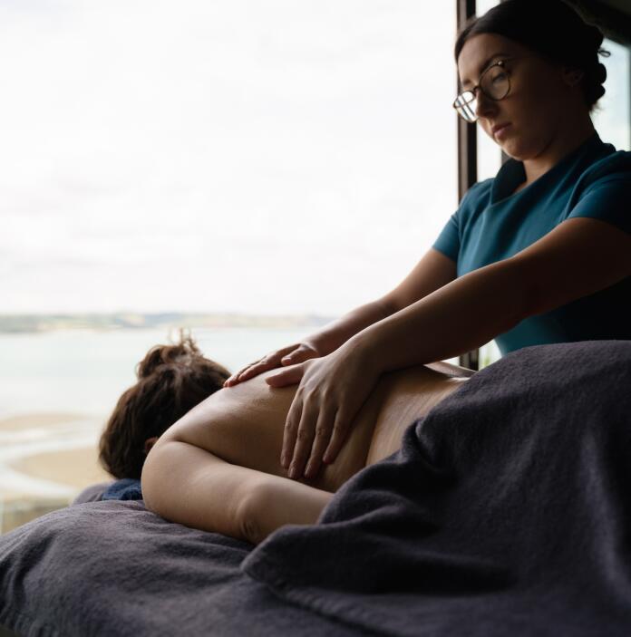 A lady having a massage on a massage table in front of sea views.