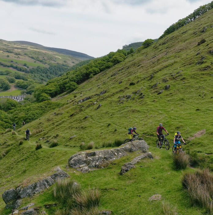A group of mountain bikers on a narrow hillside path. 