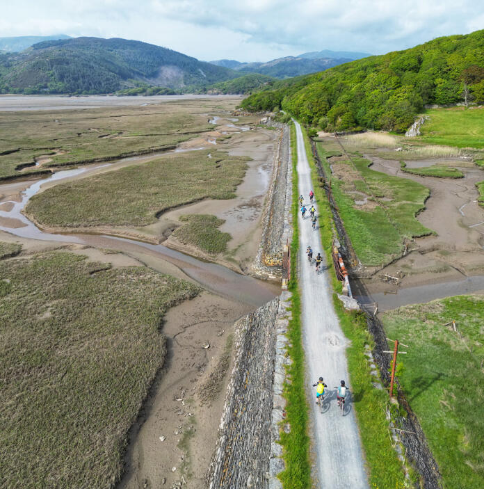 Aerial view of cyclists on an old railway line cycle path next to an estuary.