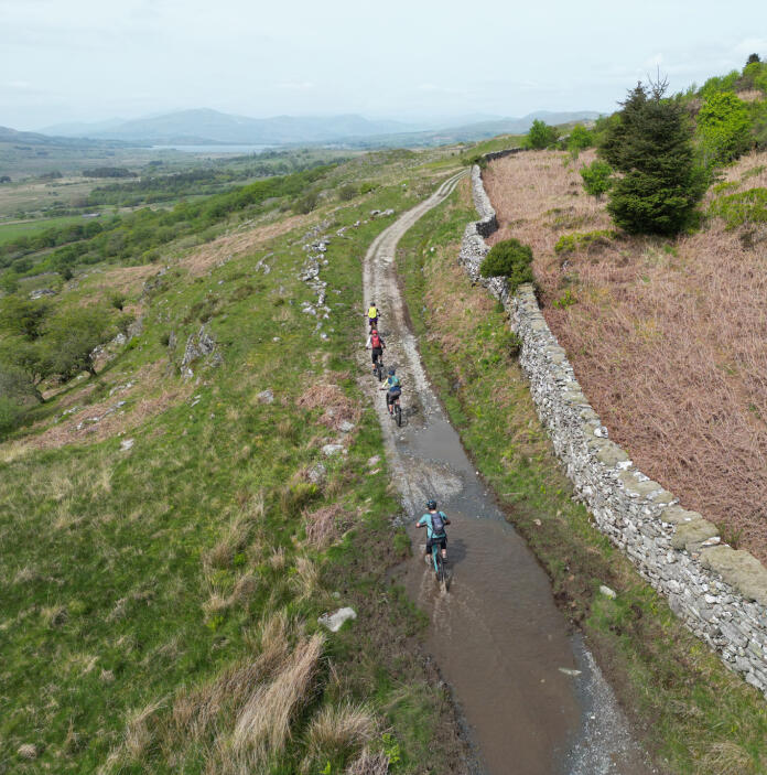 A group of mountain bikers riding through large puddles, on a hillside gravel road.