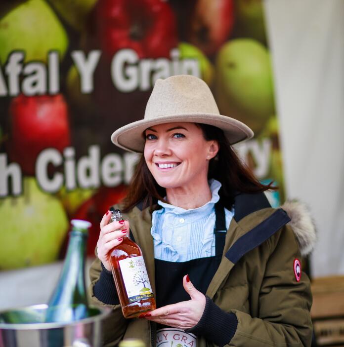 woman wearing hat and holding a bottle of cider.