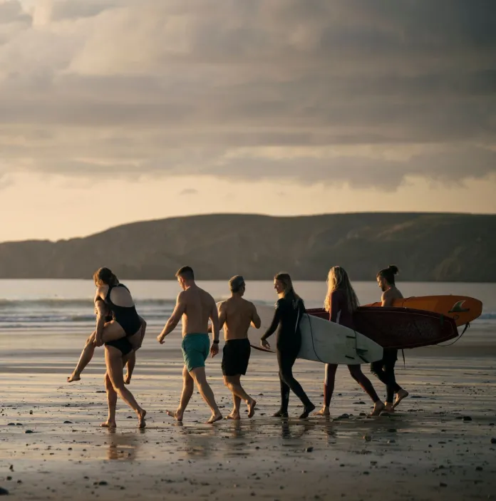 A group of friends in swimsuits walking down a beach towards the sea and carrying surfboards.