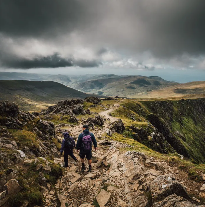 Two hikers walking along a stony path high on a mountain.