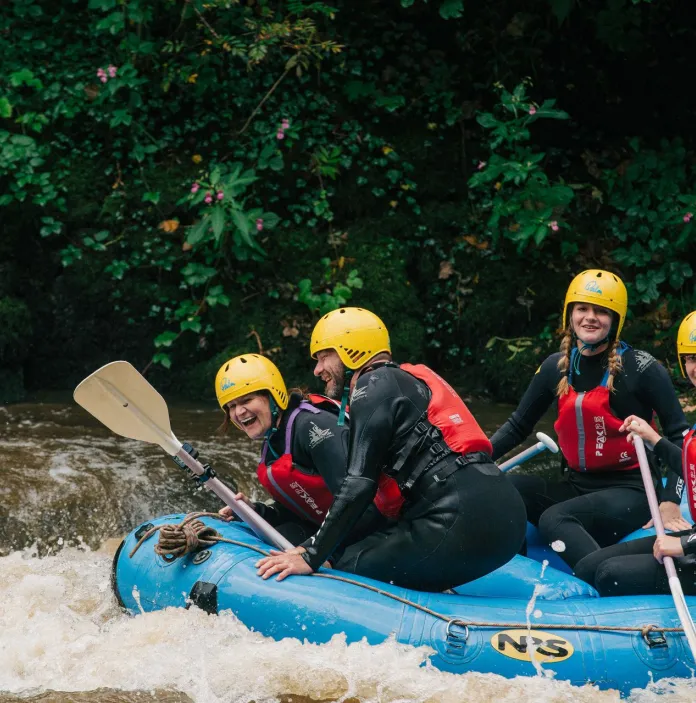 A laughing group of people on a white water raft in the middle of a river.