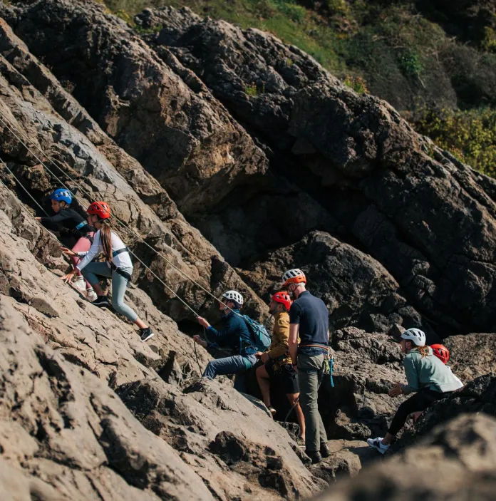 A group of people rock climbing supervised by an instructor.