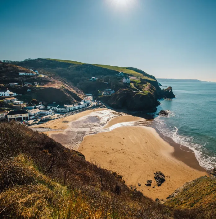 A village on the shores of a wide, golden sandy beach with cliffs either side.