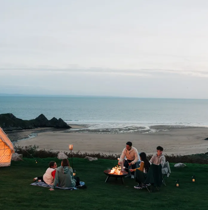 A group of people at a cliffside campsite round a firepit.