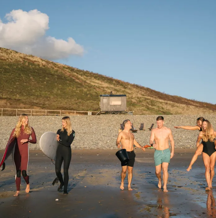 A beach with a mobile sauna, and a group of people getting ready to go surfing. 