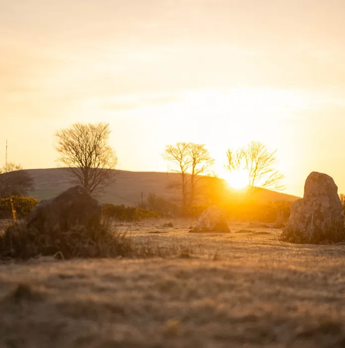 Pre-historic standing stones silhouetted with a glowing sun behind a hill.