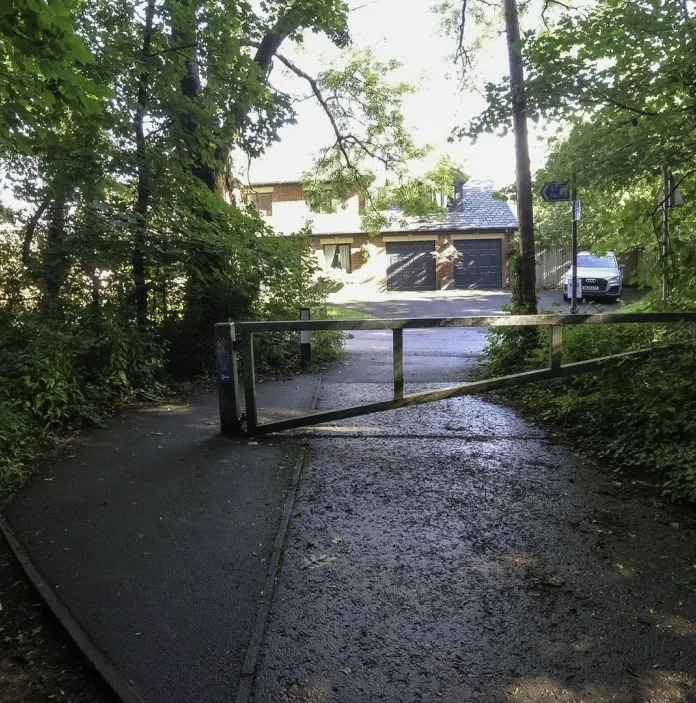 Access barrier on the Taff Trail in Cardiff, where the paved cycle route passes through woodland beside a residential area.