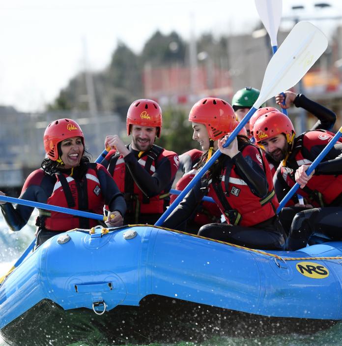 A group of people wearing helmets, wetsuits and life jackets in a white water rafting boat.