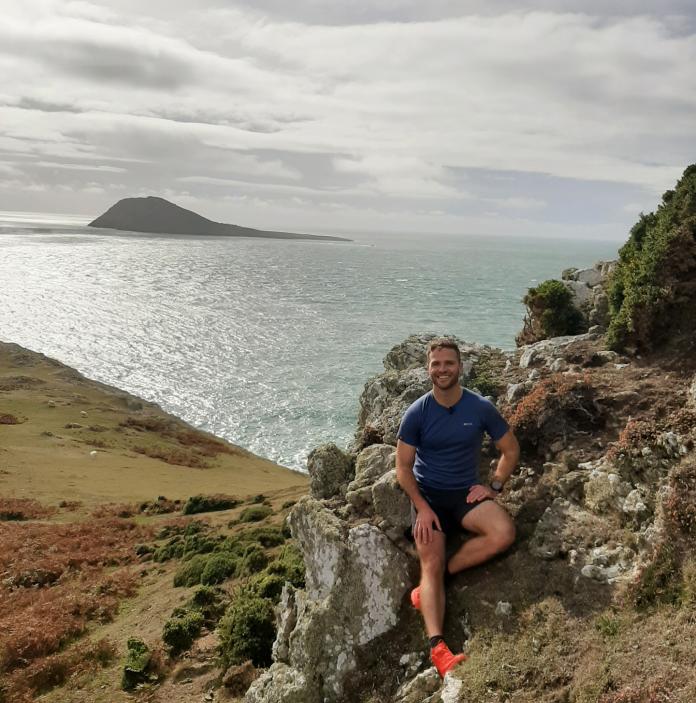 Man sat on a rock at Uwchmynydd, the soutwestern tip of the Llŷn Peninsula with Bardsey Island visible in the background.
