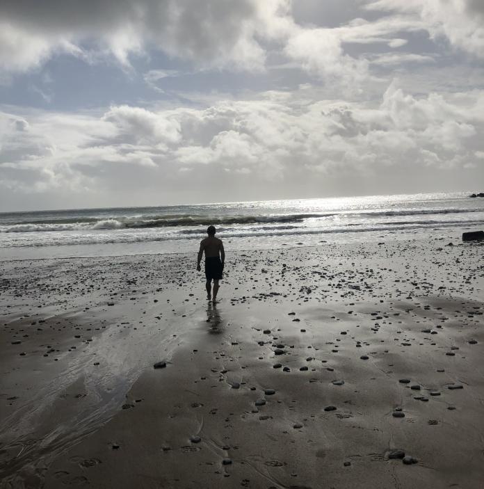 Image of a man walking across the sand on Pwll Du Bay towards the sea.