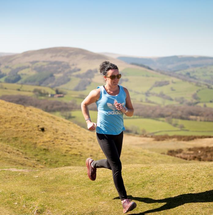 Woman running across moorland with hills in the background.