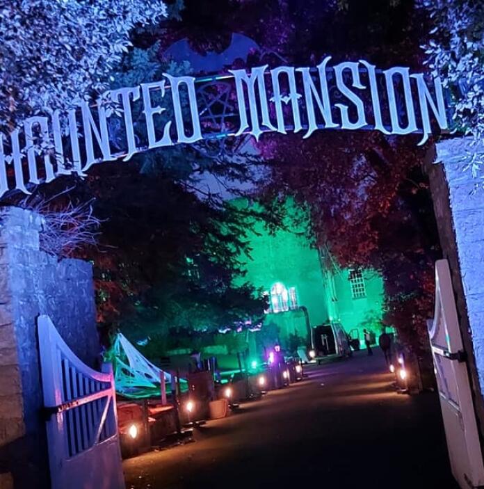 nightshot with lights and sign 'Haunted Mansion' above gate.