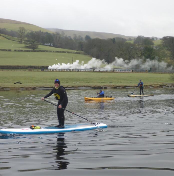 people on stand up paddle boards with steam train in background.