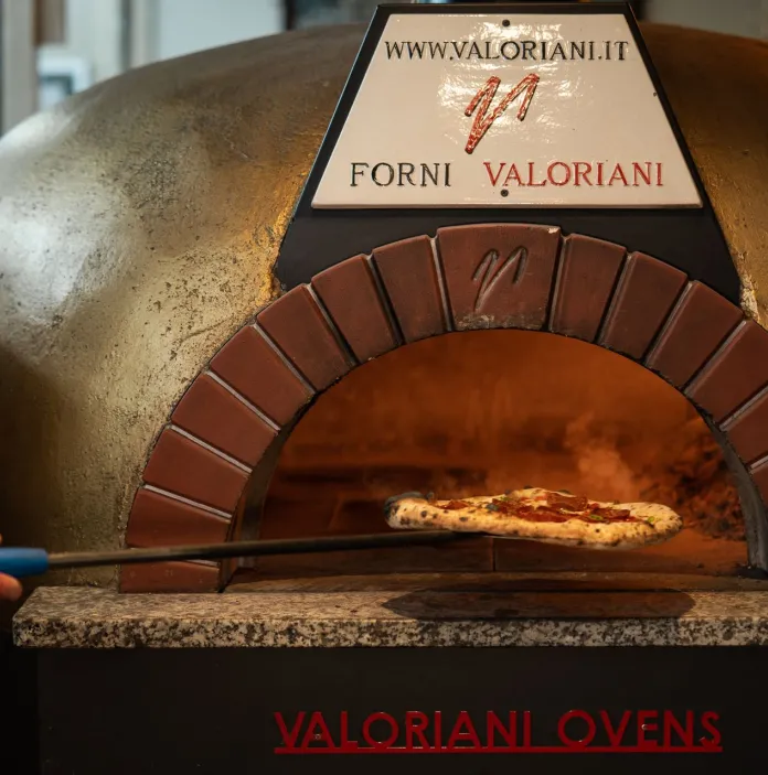 A pizza being placed in the woodfire pizza