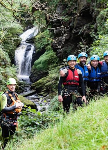 A group of people in standing near a waterfall wearing safety gear.