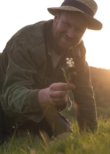 Ein Mann kniet im Gras mit einer Wildblume in der Hand.