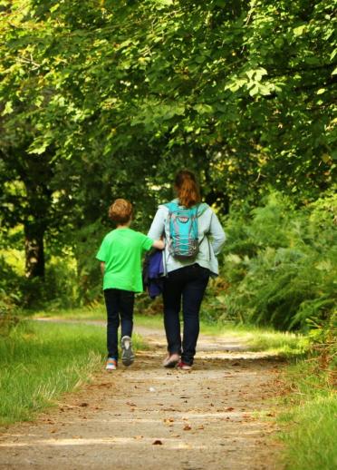 Mutter und Sohn spazieren durch einen grünen Park, mit dem Rücken zur Kamera.