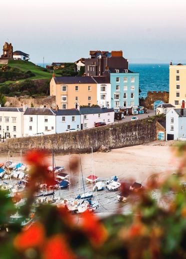 Looking down toward Tenby harbour with boats on the sand and colourful houses and the sea in the background.